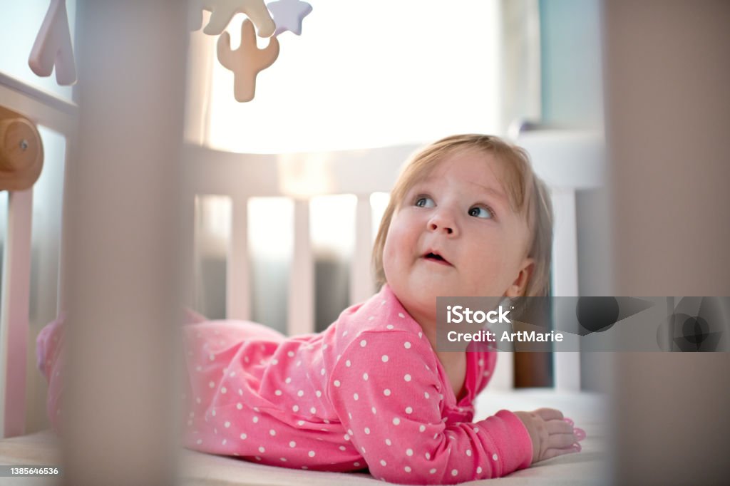 Menina feliz fofa em bodysuit rosa olhando para seu celular pendurado dentro de casa em uma manhã ensolarada - Foto de stock de Bebê royalty-free