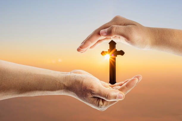 istock Human hands protecting crucifix with bright sunbeam on the colorful sunset or sunrise sky background 1385646652