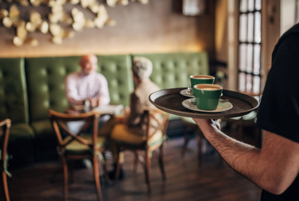 Male waiter carrying tray with cups of espresso coffee in cafe.