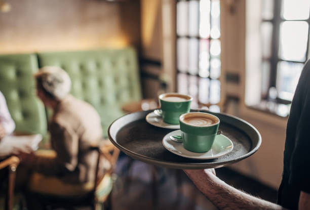 Male waiter carrying tray with cups of espresso coffee in cafe.