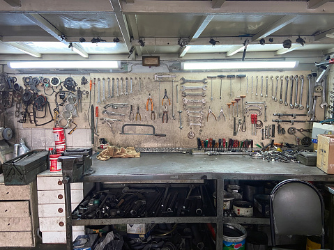 Wall of a mechanical studio with lots of tools and gears hanged on the wall and on the metal work table. Wrench, pliers, saw, screwdriver, hookup and car engine repair equipment.