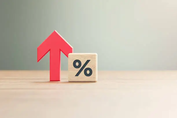 Red arrow symbol sitting next to percentage sign engraved wood block before defocused background. Horizontal composition with copy space.