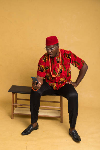 igbo traditionally dressed business man sitting down and staring at phone - nigeria african culture dress smiling imagens e fotografias de stock