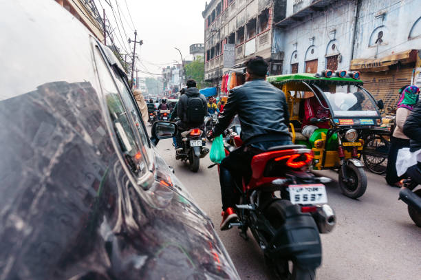 Pune Region, India - A bustling urban intersection features motorcycles and trucks waiting at a traffic signal. Tall buildings and lush trees line the streets under a clear sky.