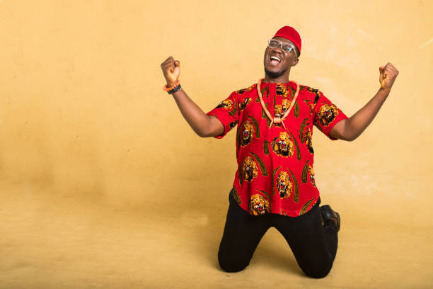 igbo traditionally dressed business man celebrate kneeling down - nigeria african culture dress smiling imagens e fotografias de stock