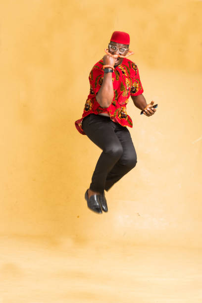 igbo traditionally dressed business man in mid air with phone in hand and fist pump - nigeria african culture dress smiling imagens e fotografias de stock