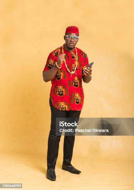 Igbo Traditionally Dressed Business Man Standing With Phone In Hand Looking Stock Photo - Download Image Now