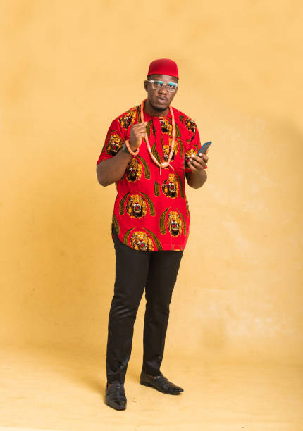 igbo traditionally dressed business man standing with phone in hand looking - nigeria african culture dress smiling imagens e fotografias de stock