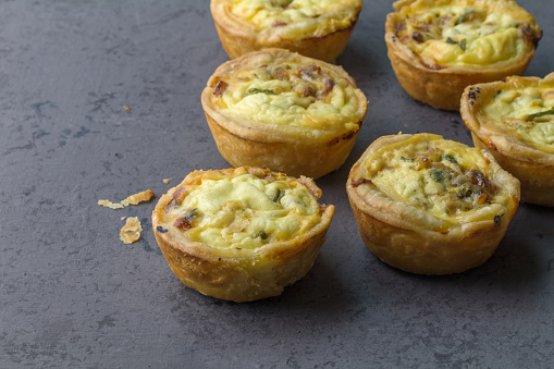 Mini ham, cheese and herb quiches freshly baked on a grey board ready to eat - close up studio photo with copy space