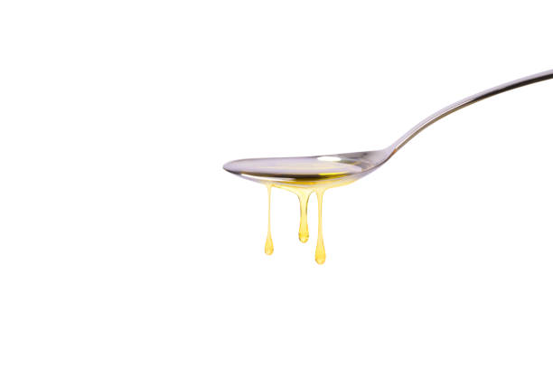 Oil drop dripping from stainless steel spoon isolated on white background. Side view, Copy space.