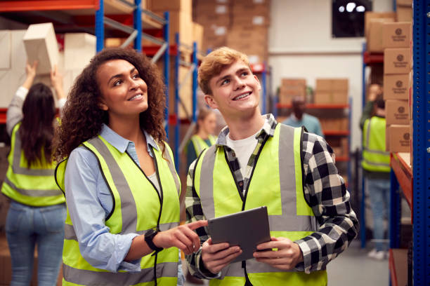 Male Intern With Team Leader Looking At Digital Tablet Inside Busy Warehouse Facility Male Intern With Team Leader Looking At Digital Tablet Inside Busy Warehouse Facility Online Freight Forwarding Courses stock pictures, royalty-free photos & images