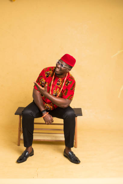 un homme d’affaires igbo vêtu traditionnellement assis expose un produit imaginaire - nigeria african culture dress smiling photos et images de collection