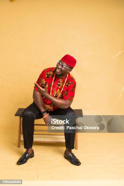 Igbo Traditionally Dressed Business Man Sitting Down Display An Imaginary Product Stock Photo - Download Image Now