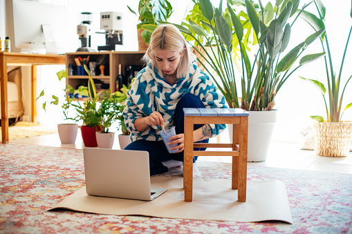 Young Woman is Painting Coffee Table With Online Workshop