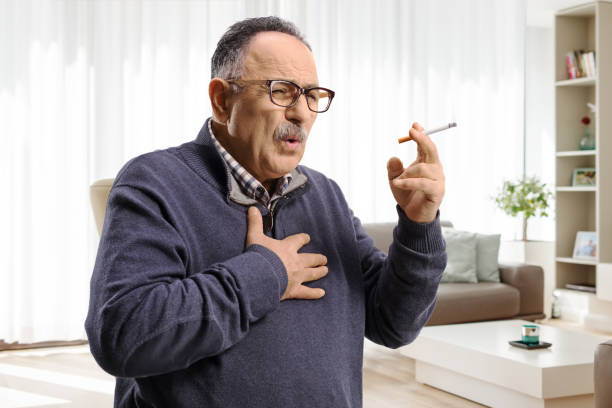 mature man smoking and coughing at home - nicotine healthcare and medicine smoking issues lifestyles imagens e fotografias de stock