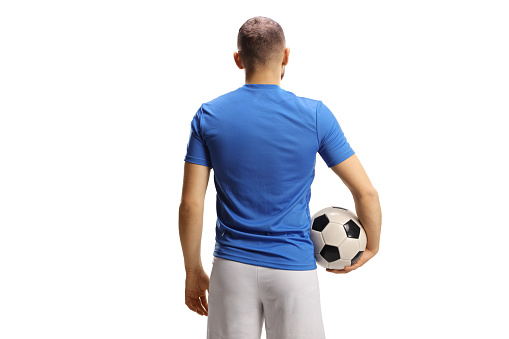 Rear view shot of a soccer player in a blue jersey and white shorts holding a ball isolated on white background