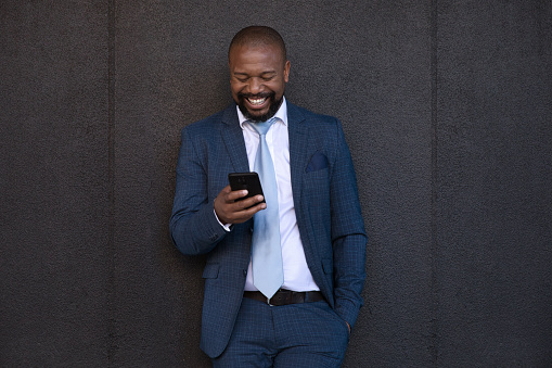 Happy businessman on his phone standing outside against grey wall