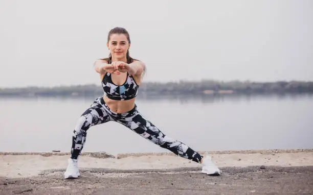 Photo of Woman doing walking lunges outdoors overlooking the river. Fitness, sport and healthy lifestyle concept.