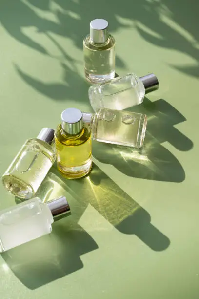 Photo of Glass bottle cosmetics with organic aroma oil for beauty or skin care on green background, natural sun light and shades.
