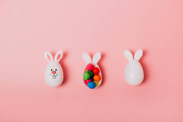 istock Top view festive Easter pink background with funny bunny eggs container filled with candy chocolate eggs. Bunny rabbit symbol. Easter egg hunt. Creative Easter. Flat lay. Copy space. 1385685530