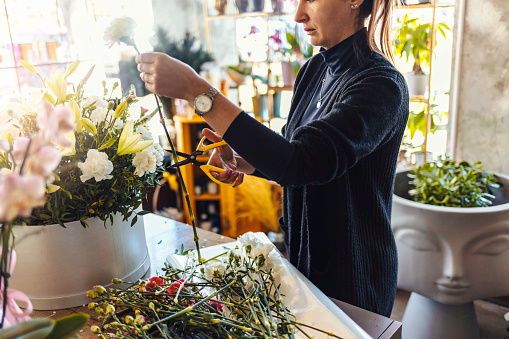 Concept of flower arranging, making beautiful bouquets with your own hands. Shot of unrecognizable woman entrepreneur arranging bouquet of a fresh flowers and plants at her workshop studio with copy space on desk.