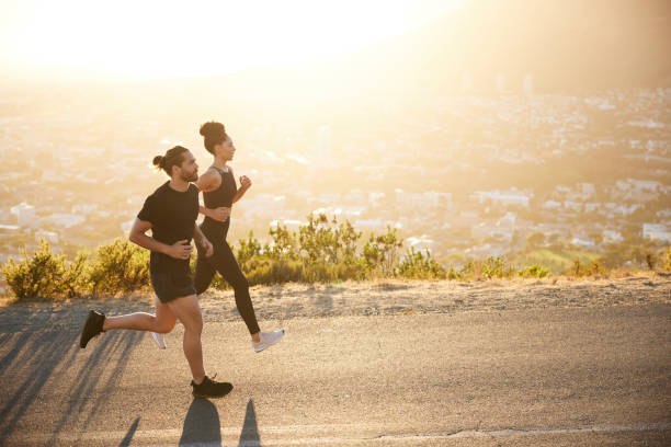 zwei fitte junge leute joggen gemeinsam auf einer panoramastraße - rennen stock-fotos und bilder