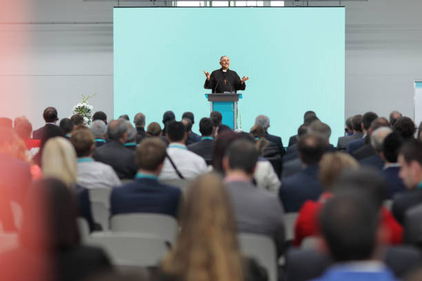 istock Priest talking on a speaker podium in front of audience 1385690276