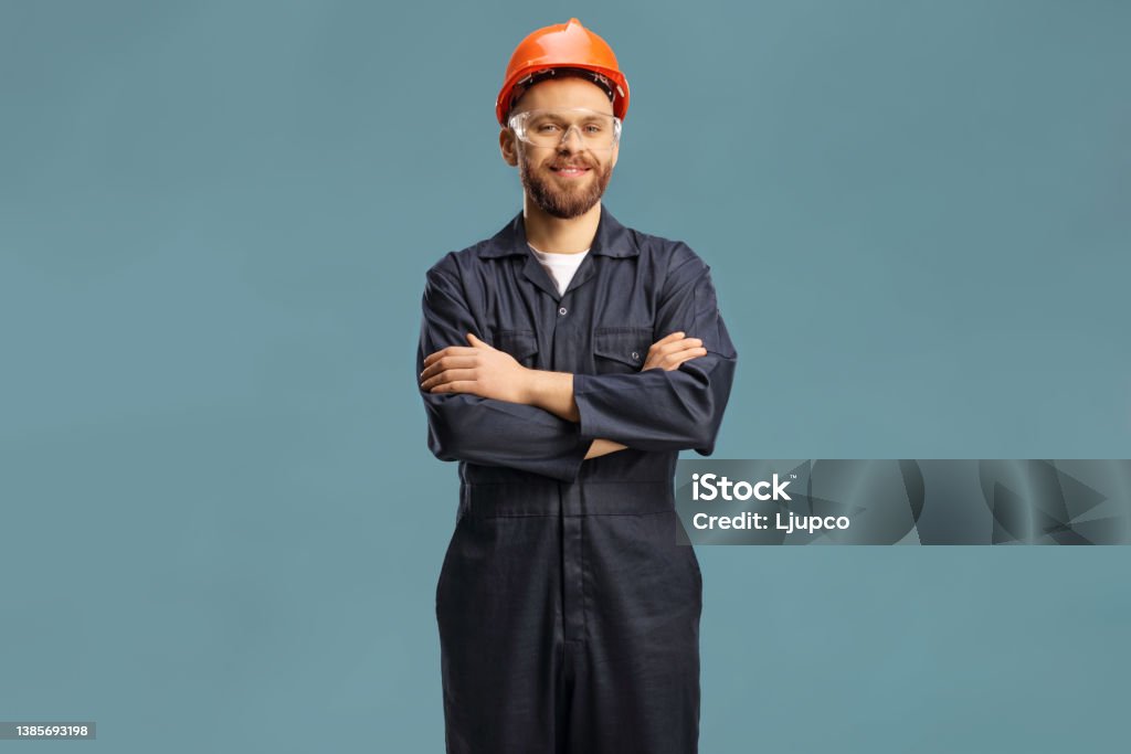 Technician in a uniform with a helmet and goggles Technician in a uniform with a helmet and goggles isolated on blue background Coveralls Stock Photo