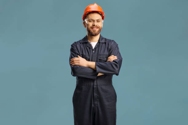 Technician in a uniform with a helmet and goggles Technician in a uniform with a helmet and goggles isolated on blue background maintenance worker stock pictures, royalty-free photos & images