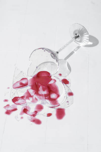 istock Broken glass with red wine on a table with white tiles 1385694123