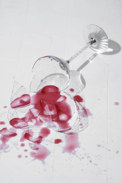 istock Broken glass with red wine on a table with white tiles 1385694128