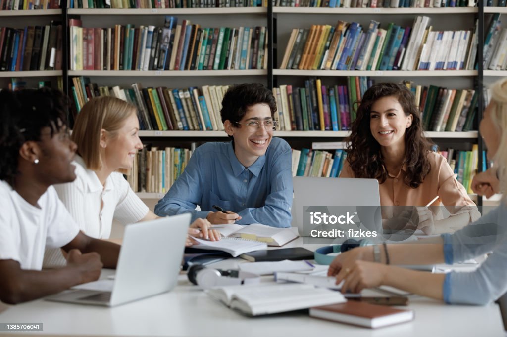 Happy group of diverse multiracial students studying at library. Happy group of diverse multiracial friendly students talking, discussing new school project ideas together, enjoying preparing for examinations, doing common research in library, education concept. Student Stock Photo