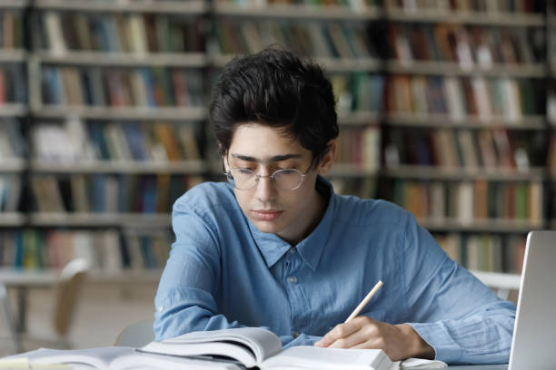 fokussierter beschäftigter junger männlicher jüdischer student, der in der bibliothek studiert. - male education college student nerd stock-fotos und bilder