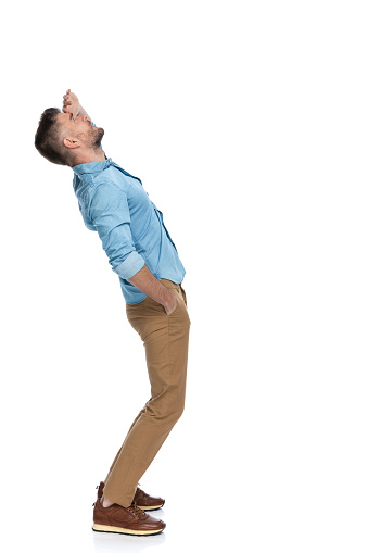 side view of casual guy with hand in pocket holding hand to forehead and trying to see something far away in the air on white background