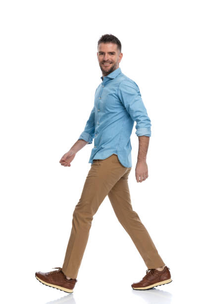 sexy middle aged man with sneakers in denim shirt with chino pants stepping and smiling on white background