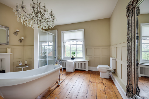 Traditional bathroom with roll top bath within former old rectory with fireplace, exposed timber floors, shower cubicle, large chandelier and mirror.