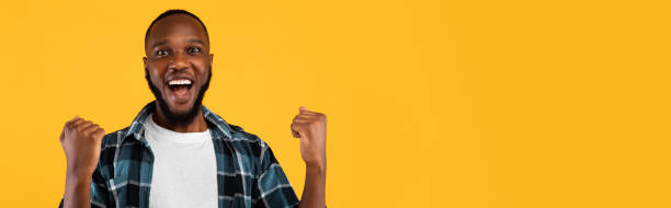 istock Excited Black Guy Shaking Fists Posing Over Yellow Background, Panorama 1385710584