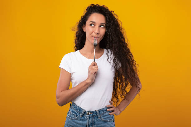 portrait of smiling latin lady holding fork in mouth - esfomeado imagens e fotografias de stock