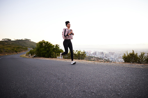 Fit young woman in sportswear out for a jog alone on a scenic road overlooking a city in the early morning