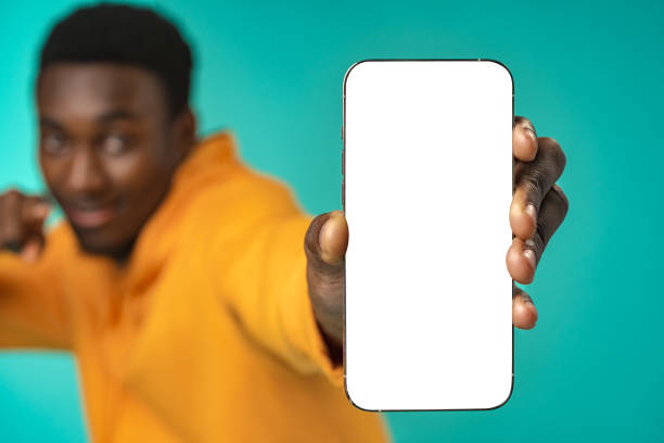 istock Smiling casual black man pointing at blank white cell phone screen in studio 1385715247