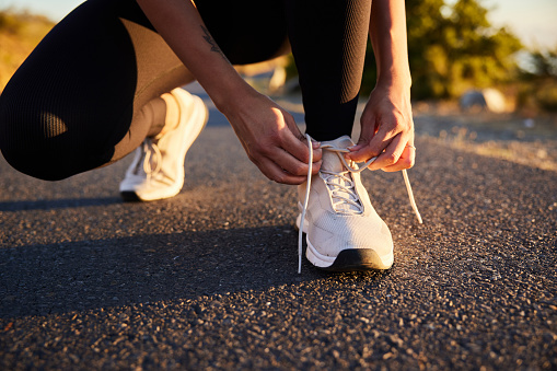 istock Woman tying up her running shoes outside on an asphalt road 1385715287