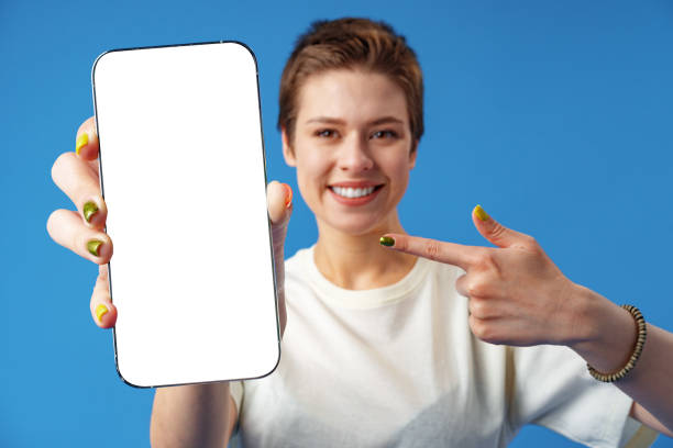 istock Portrait of a young woman showing blank screen mobile phone while standing over blue background 1385715744