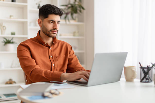 istock Arab man using laptop sitting at desk in office 1385716339