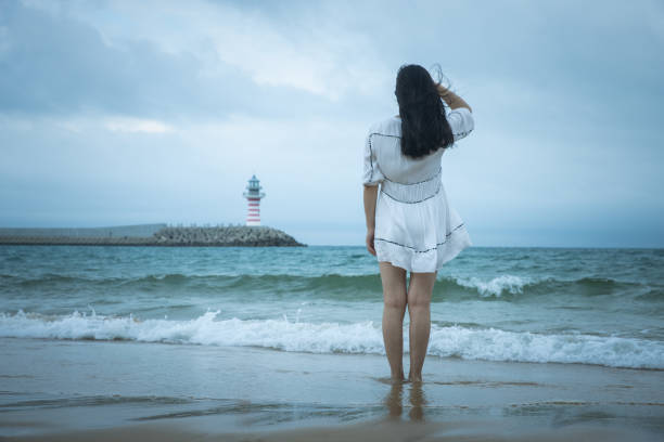 woman standing by the sea looking at the lighthouse