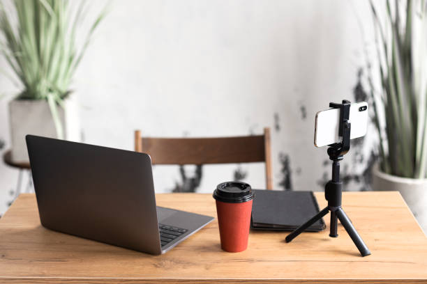 istock Comfortable workspace for office manager, business or freelancer in a stylish room with green plants for remote work on a laptop and online video conference using a mobile phone on a tripod 1385720580