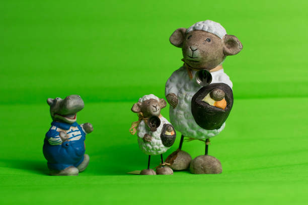 Two same, bigger and smaller, white fluffy sheep standing side by side holding basket with Easter eggs with little hippo wearing blue pants and big smile on his face, green isolated background.