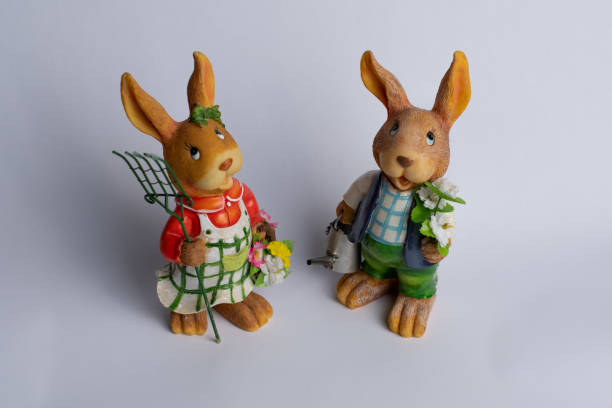 istock Two Easter rabbits standing side by side, holding gardening stuff and spring plants, isolated on white background. High angle view. 1385720751