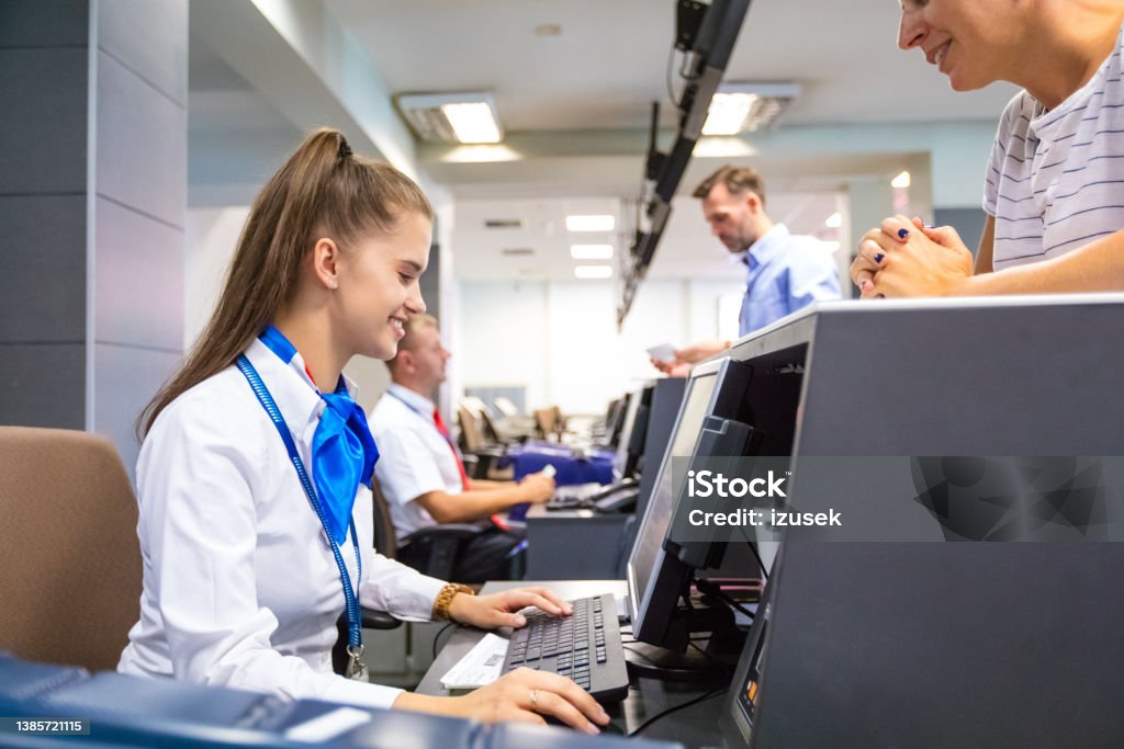 Airline attendant doing check-in for flight at airport Passengers standing at check-in counter at the airport and talking with airline attendants. Manager Stock Photo