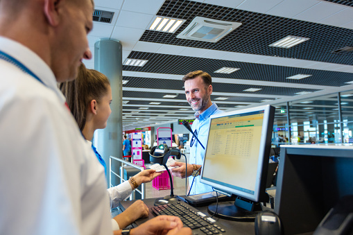 Man standing at check-in counter at the airport and talking with young woman. Defocused crowd in the background.