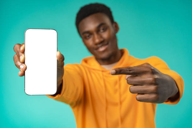istock Smiling casual black man pointing at blank white cell phone screen in studio 1385722331